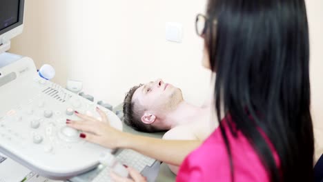 Close-up-view-of-young-female-doctor-with-long-hair-in-rose-uniform-is-screaning-her-patient's-heart-with-ultrasonography,-looking-at-the-screen,-and-consulting.