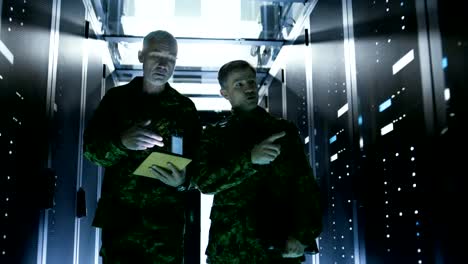 Two-Soldiers-Walking-in-Data-Center-Corridor.-One-Holds-Tablet-Computer,-They-Have-Discussion.-Rows-of-Working-Data-Servers-by-their-Sides.