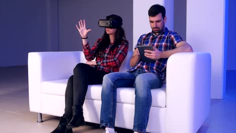 Hi-Tech-paar:-Mädchen-mit-virtual-Reality-Gerät-während-der-junge-Mann-etwas-auf-seine-digital-Tablette-eingeben