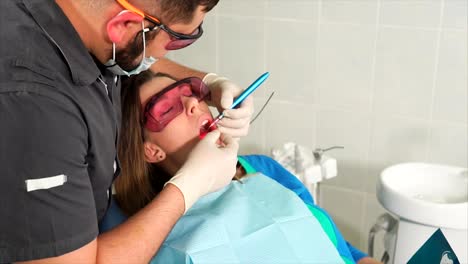 Médico-ortodoncista-con-vidrios-blanquea-los-dientes-de-una-mujer-joven-con-un-láser