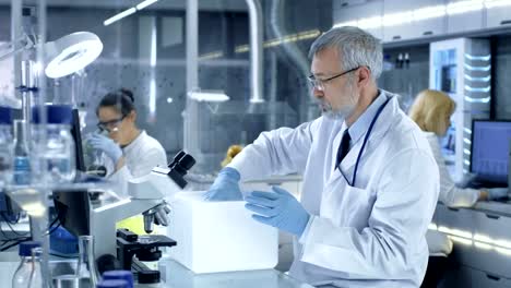 Senior-investigación-científico-abre-refrigerador-caja-médica-toma-un-plato-de-Petri,-con-muestras-y-examina.-Trabaja-en-un-centro-de-laboratorio-moderno-ocupado.