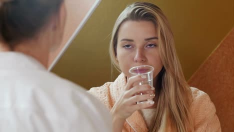 Lächelnde-Frau-nimmt-Medizin-und-ein-Glas-Wasser-im-Krankenhaus