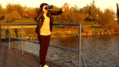 Junge-Frau-mit-einer-virtual-Reality-Brille-auf-der-Mole-bei-Sonnenuntergang