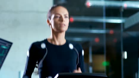 Beautiful-Woman-Athlete-with-Electrodes-Connected-to-Her-Body-Runs-on-a-Treadmill-in-a-Sport-Science-Laboratory.-In-the-Background-High-Tech-Laboratory-with-Monitors-Showing-EKG-Readings.
