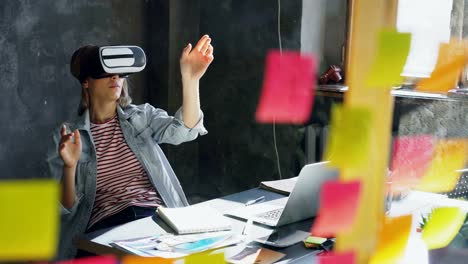 Attractive-young-woman-is-sitting-at-table-and-wearing-virtual-reality-glasses.-She-is-moving-hands-and-and-having-VR-experience-in-modern-lof-office