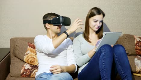 Man-using-virtual-reality-device-while-woman-typing-on-digital-tablet