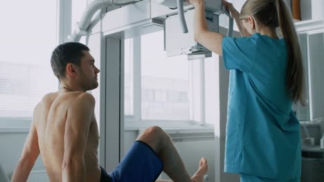 In-the-Hospital,-Man-Sitting-on-a-Bed,-Female-Technician-adjusts-X-Ray-Machine-for-Scanning-His-Leg-for-Injury.-Scanning-for-Fractures,-Broken-Limbs,-Cancer-or-Tumor.-Modern-Hospital-with-Technologically-Advanced-Medical-Equipment-and-Professional-Personn