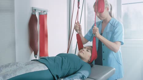 Physiotherapeut-hilft-Patientin-mit-Trauma,-rehabilitativen-Physiotherapie-auf-eine-spezielle-Aufhängung-Seilsystem-unterziehen.-Hals,-Rücken,-Kopf-Schmerzen-lindern.-Moderne-Klinik-mit-den-meisten-erweiterte-Rehabilitation-Verfahren.