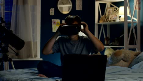 Boy-using-VR-glasses-and-laptop-on-bed