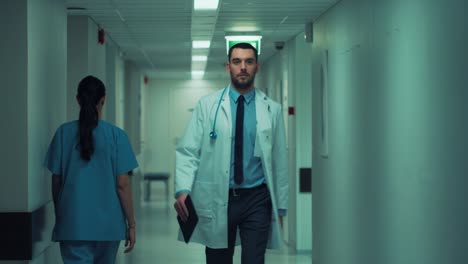 Determined-Handsome-Doctor-Wearing-White-Coat-with-Stethoscope-Walks-Through-Hospital-Hallway-in-Slow-motion.-Modern-Bright-Clinic-with-Professional-Staff.