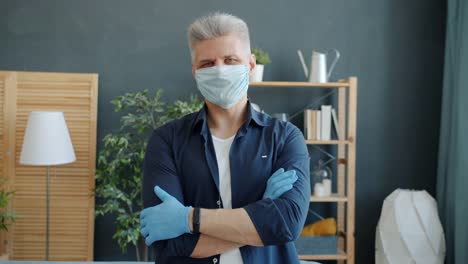 Portrait-of-mature-guy-in-face-mask-and-gloves-standing-in-apartment-during-pandemic