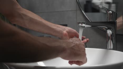 Man-washes-hands-in-sink-with-foam-to-wash-skin-and-water-flows-through-hands.-Concept-of-health,-cleaning-and-preventing-germs-and-coronavirus-from-contacting-hands.-Coronavirus-pandemic-prevention