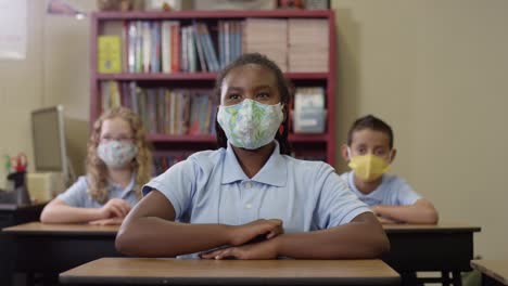 Grundschulkinder-tragen-Masken-im-Unterricht,-als-schwarzes-Mädchen-ihre-Hand-hebt