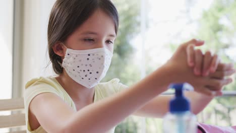 Girl-wearing-face-mask-sanitizing-her-hands-at-home