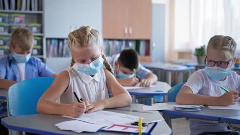 Schüler-in-medizinischen-Masken,-die-Schularbeiten-am-Schreibtisch-im-Klassenzimmer-sitzen,-Kinder-wieder-in-der-Schule-nach-covid-19-Quarantäne-und-Sperrung