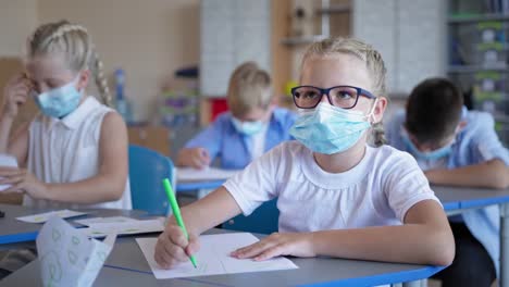 Schüler-wieder-in-der-Schule-nach-Quarantäne-und-Sperrung,-Schülerin-in-Brille-und-medizinische-Maske-tun-Klassenarbeit-sitzen-am-Schreibtisch