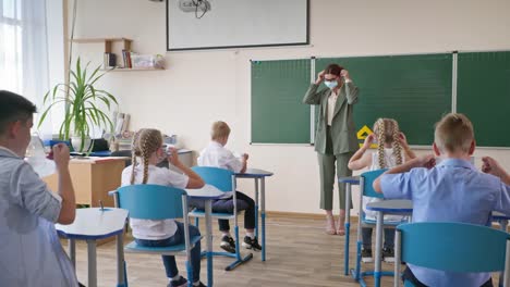 neues-normales-Leben-nach-COVID,-Lehrerin-in-der-Nähe-von-Tafel-zeigt-einer-Gruppe-von-Kindern,-wie-man-medizinische-Maske-auf-Gesicht-während-einer-Lektion-im-Klassenzimmer