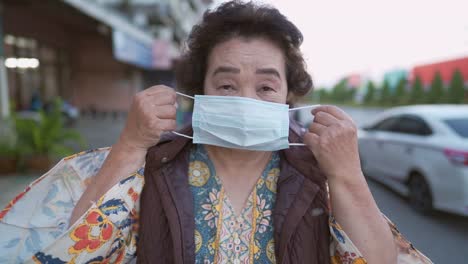 Asian-Senior-lady-wearing-protective-face-mask-standing-on-the-roadside-infectious-diseases-prevention-during-Corona-virus-covid-19-social-distancing,-risk-of-illness-protection,-waiting-for-vaccine