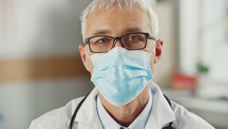 Close-Up-Portrait-of-a-Senior-Caucasian-Male-Doctor-or-Surgeon-Wearing-a-Protective-Face-Mask-and-Glasses.-Middle-Aged-Scientist-Calmly-Looking-at-Camera.-Medical-Care-Specialist-in-Covid-19-Reality.