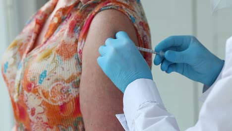 Close-up--woman-is-shoulder-and-a-doctor's-hands-in-medical-gloves-make-a-vaccine-against-the-Covid-19-coronavirus.-The-doctor-holds-a-syringe-and-gives-an-injection-to-a-senior-patient-wearing-.
