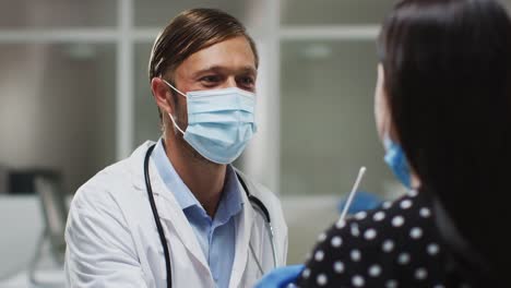Kaukasischer-männlicher-Arzt-trägt-Gesichtsmaske-und-Handschuhe-unter-Tupfer-Test-vom-Patienten