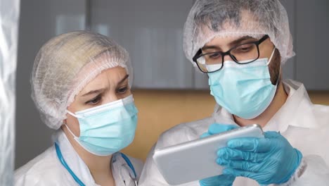 Medical-team-of-doctors-in-white-coats,-gloves-and-protective-masks-discuss-patients-diagnosis-on-digital-tablet-in-hospital.-Treatment-concept-for-coronavirus,-covid-19