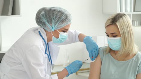 Medical-nurse-in-safety-gloves-and-protective-mask-vaccinates-female-patient-in-clinic.-Doctor-injects-medicine-into-hand-from-syringe.-Covid-19,-coronavirus-vaccine