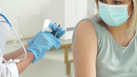 Close-up-of-medical-nurse-in-gloves-and-mask-vaccinates-female-patient-in-clinic.-Doctor-injects-medicine-into-hand-from-syringe-and-applies-medical-patch.-Covid-19,-coronavirus-vaccine