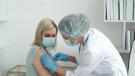 Una-enfermera-médica-con-guantes-vacuna-a-la-paciente-con-máscara-en-el-hospital.-El-médico-inyecta-medicamentos-en-la-mano-a-partir-de-jeringa.-Vacuna-contra-el-coronavirus