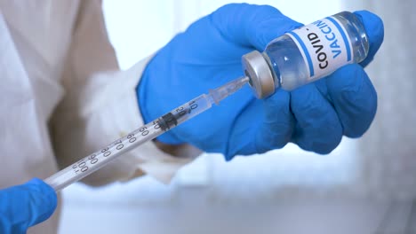 Doctor-hands-with-blue-surgical-gloves-holding-syringe-and-COVID-19-vaccine.-COVID-19-vaccine-concept.-Health-and-medical-concept.-Selective-focus,-Close-up-syringe-and-vaccine-dose.-Macro-4K-video.