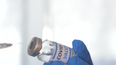 Doctor-hands-with-blue-surgical-gloves-holding-syringe-and-COVID-19-vaccine.-COVID-19-vaccine-concept.-Health-and-medical-concept.-Selective-focus,-Close-up-syringe-and-vaccine-dose.-Macro-4K-video.