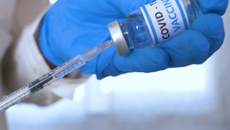 Doctor-hands-with-blue-surgical-gloves-holding-syringe-and-COVID-19-vaccine.-COVID-19-vaccine-concept.-Health-and-medical-concept.-Selective-focus,-Close-up-syringe-and-vaccine-dose.-Macro-4K-video.