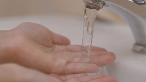 Zeitlupe.-Nahaufnahme-der-menschlichen-Hand-unter-dem-Strom-von-reinem-Wasser-aus-Hahn.-Child-Palm-Under-Stream-of-Water-Slow-Motion.-Kleines-Mädchen-im-Badezimmer-zu-Hause-Überprüfen-Temperatur-berührenfließendes-Wasser.