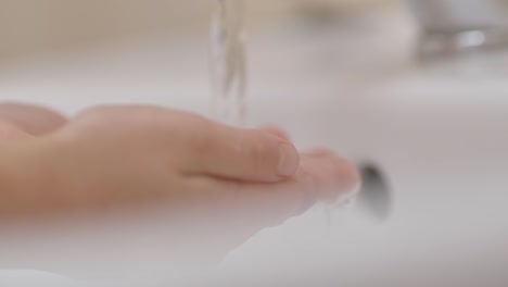 Zeitlupe.-Nahaufnahme-der-menschlichen-Hand-unter-dem-Strom-von-reinem-Wasser-aus-Hahn.-Child-Palm-Under-Stream-of-Water-Slow-Motion.-Kleines-Mädchen-im-Badezimmer-zu-Hause-Überprüfen-Temperatur-berührenfließendes-Wasser.