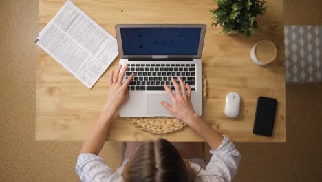 The-girl-works-remotely-via-the-Internet.-Sitting-at-his-laptop.-Top-view.-Wooden-table.-The-concept-of-e-learning-from-home.-Selective-Focus