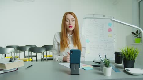 Woman-professor-sitting-at-table-and-lecturing-online-at-class.-Female-English-teacher-in-glasses-speaking-on-smartphone-camera.-Education-concept.-Quarantine-concept.-Study-by-internet.