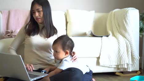 Yong-Mutter-arbeitet-mit-Laptop-zu-Hause-und-ihr-Sohn-spielt-neben-ihr.