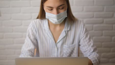 Una-chica-con-un-pejama-a-rayas-contra-una-pared-de-ladrillos-con-una-máscara-médica.-Funciona-de-forma-remota.-Primer-plano.-Enfoque-selectivo.-vista-frontal