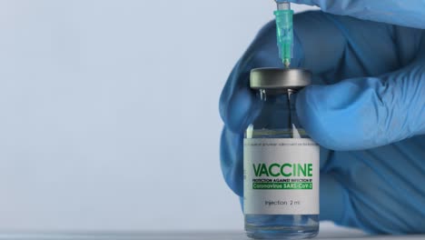 Doctor-fills-syringe-from-flask-of-vaccine-for-coronavirus-COVID-19-cure-before-injection.-Vaccination-concept-pandemic.-Needle-pierces-top-cap-and-gets-inside-vial.-Medical-gloves.-Macro-wide-shot