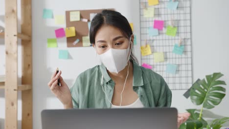 Asia-businesswoman-wearing-medical-face-mask-using-laptop-talk-to-colleagues-about-plan-in-video-call-while-working-from-home-at-living-room.