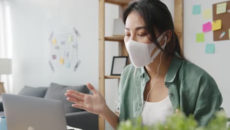 Asia-businesswoman-wearing-medical-face-mask-using-laptop-talk-to-colleagues-about-plan-in-video-call-while-working-from-home-at-living-room.