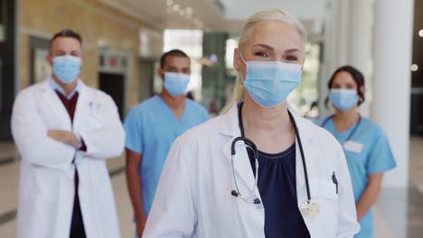 Zufriedener-Oberarzt-trägt-Gesichtsmaske-mit-Team-im-Hintergrund