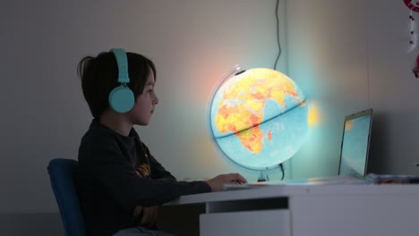 Hermoso-niño-con-auriculares-usando-computadora-portátil-mientras-estudia-en-el-escritorio-en-casa-durante-el-coronavirus