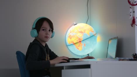 Hermoso-niño-con-auriculares-usando-computadora-portátil-mientras-estudia-en-el-escritorio-en-casa-durante-el-coronavirus