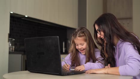 Distance-learning-concept.-girl-schoolgirl-with-her-mom-learns-online-using-a-laptop,-making-notes-in-a-notebook.-Online-video-course,