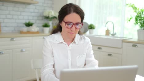 Young-woman-girl-student-freelancer-businesswoman-working,-typing-text-on-keyboard-using-laptop-computer-at-home-kitchen