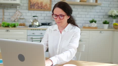 Young-woman-girl-student-freelancer-businesswoman-working,-typing-text-on-keyboard-using-laptop-computer-at-home-kitchen