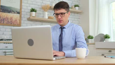Young-man-male-student-freelancer-businessman-working,-typing-text-on-keyboard-using-laptop-computer-at-home-kitchen