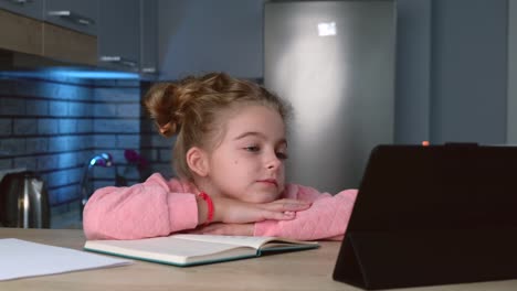 Una-pequeña-colegiala-está-teniendo-clases-en-línea-en-una-tableta-mientras-hace-su-tarea-escuchando-al-maestro