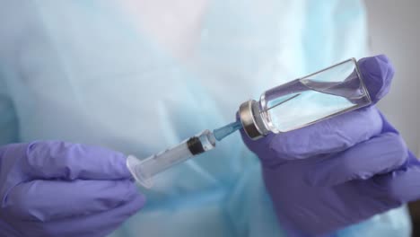 Doctor's-hands-in-medical-gloves-filling-syringe-with-vaccine-from-glass-bottle